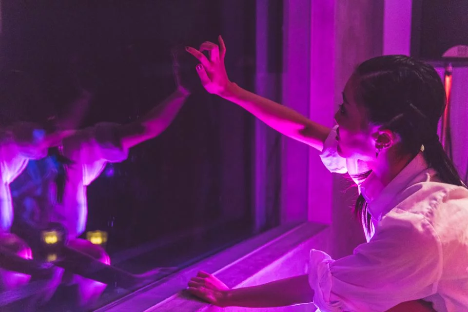 Drenched in purple light, Eriko extends her arm